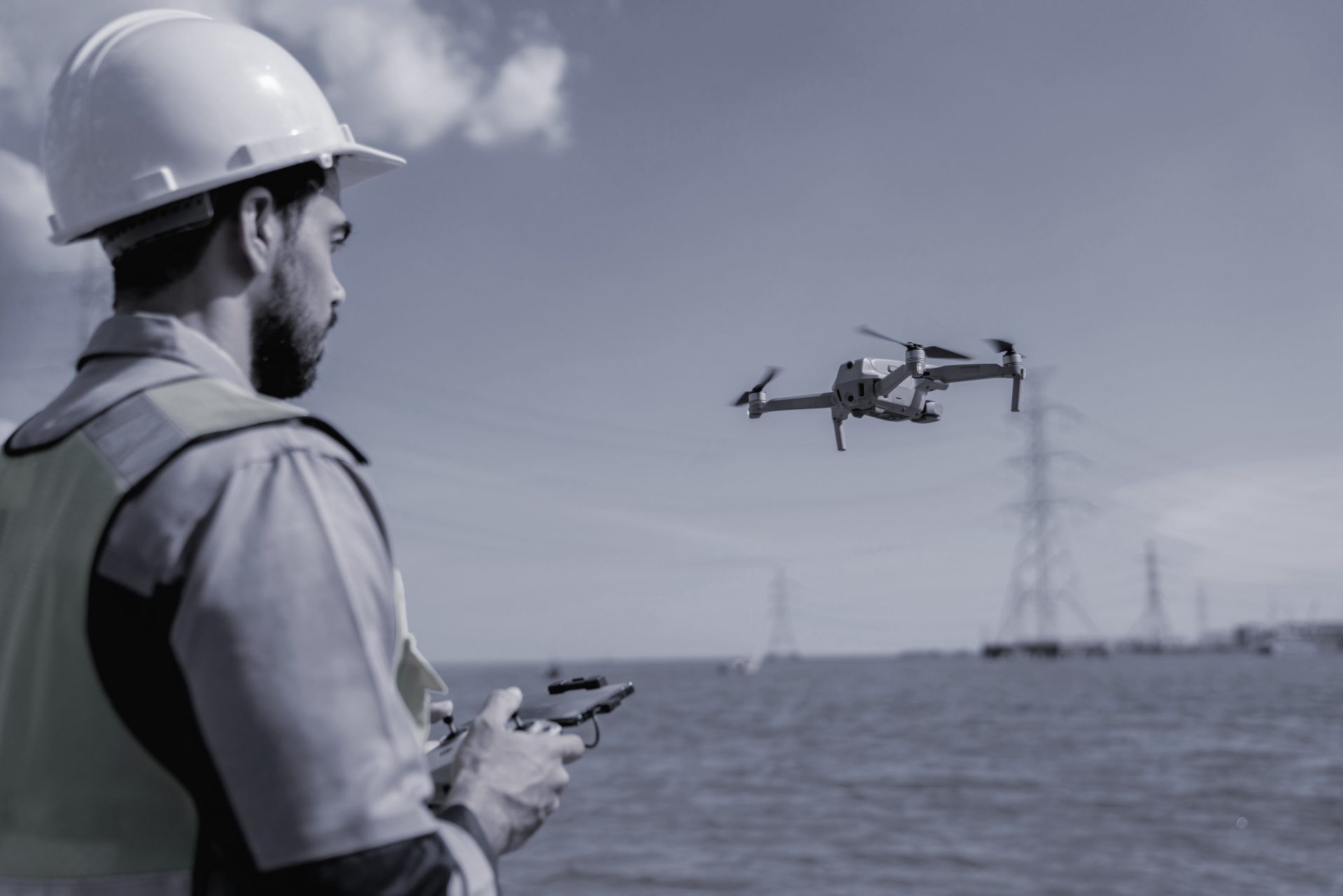 Worker in hard hat flying a drone and inspecting and surveying electrical power lines