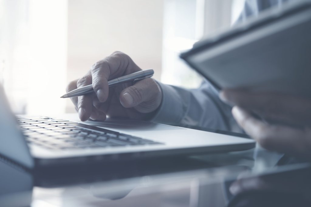 Man holding a pen resting his hand on an open laptop